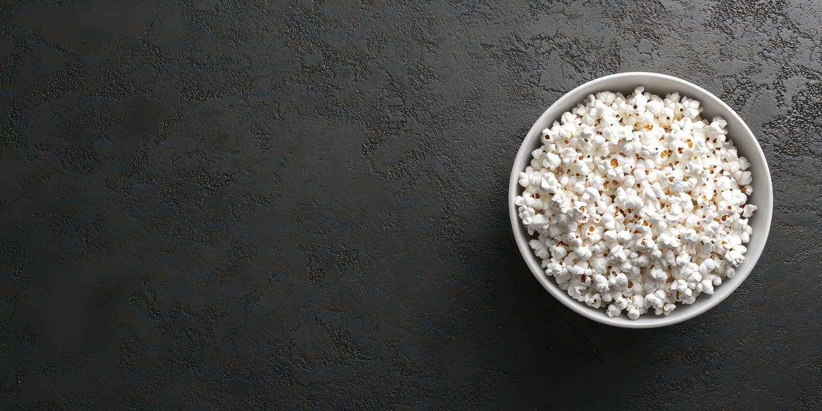 Bowl of freshly popped popcorn on a dark stone background ready for movie night or a snack at home